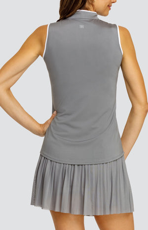 Model wearing a gray sleeveless top with an open v neck collar with white accents and side vents. Paired with a matching mesh pleated skort with solid undershorts.