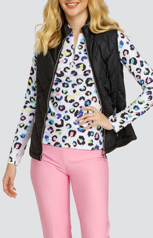 Model wearing a long sleeve top with a spotted animal print in yellow, blue, turquoise, pink and black on a white background, a black puffer vest and solid pink pants.