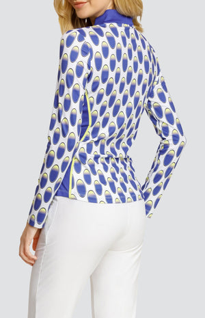Model wearing a long sleeve golf top with an oval pattern in blue and yellow on a white background, and solid white pull on golf pants.